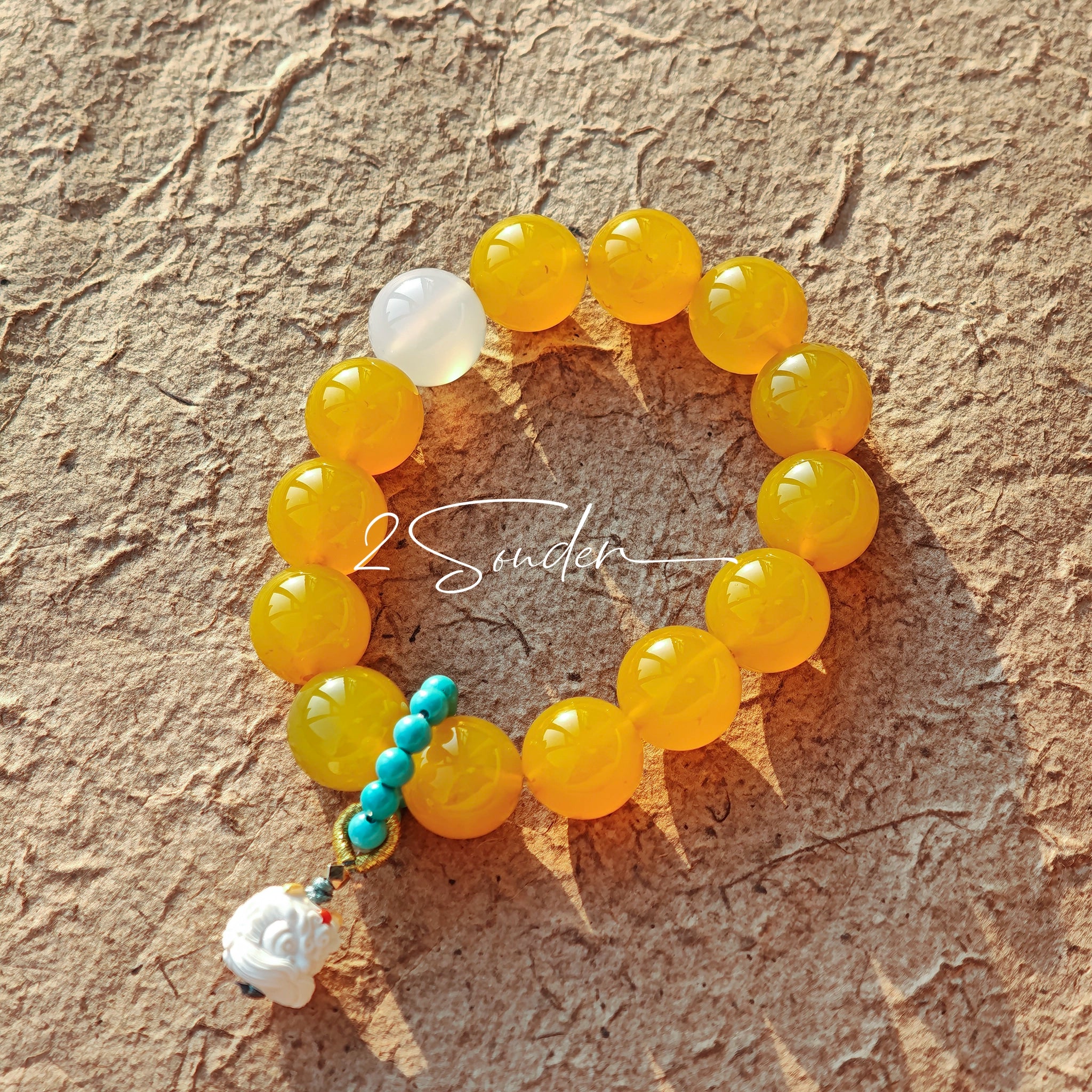 This handcrafted bracelet features glossy 14mm yellow agate beads paired with one white agate bead. It is accented with turquoise beads and finished with a detailed mammoth ivory guardian lion charm, bringing a warm vintage ethnic vibe.
