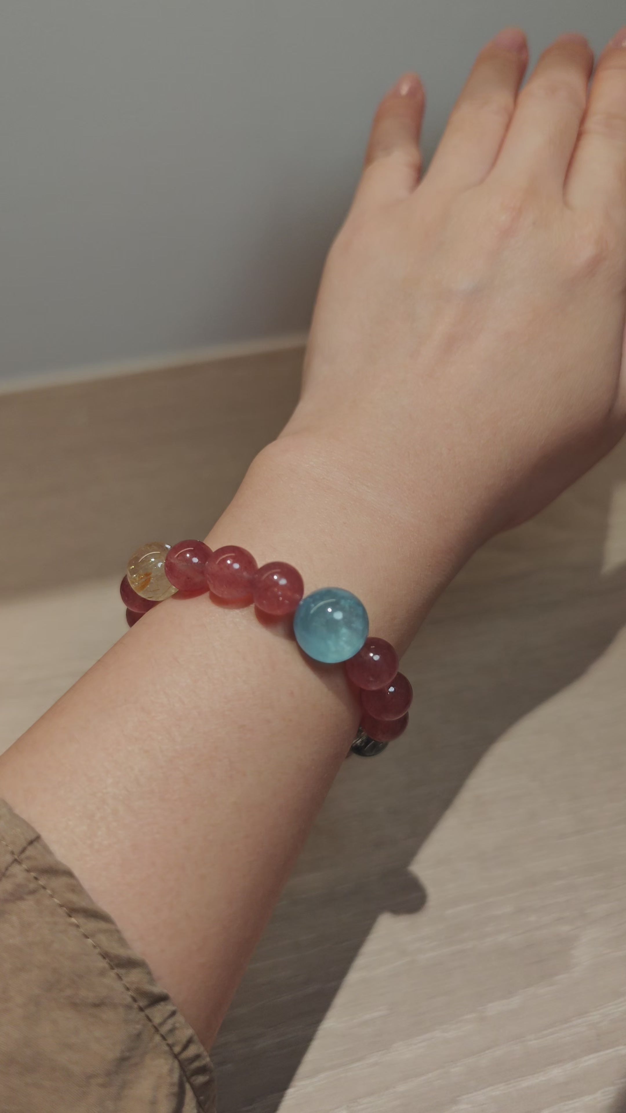 This bracelet is centered around a prominent round light blue aquamarine bead, surrounded by rich reddish-brown strawberry quartz beads. It is accented with clear crystal, black rutilated quartz, and golden rutilated quartz beads, along with delicate gold spacers, creating a harmonious natural stone design.