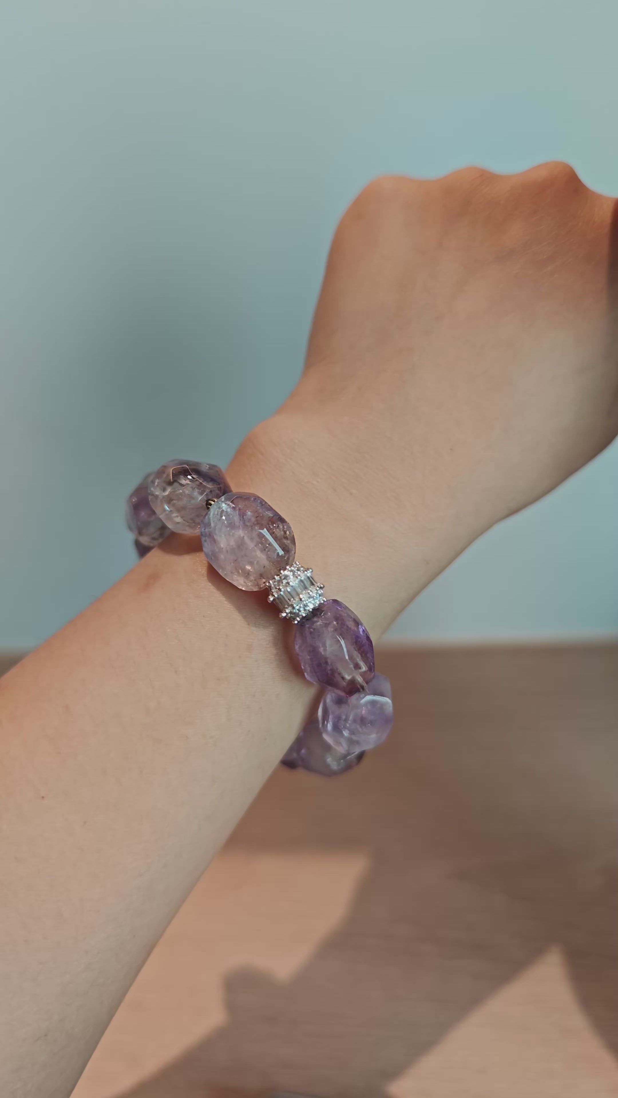 This exquisite Super Seven bracelet showcases irregularly faceted beads in a captivating blend of soft lavender and smoky purple hues, each displaying unique natural inclusions that catch the light beautifully. The polished crystals are seamlessly interspersed with tiny metallic spacer beads, culminating in an ornate silver-tone decorative bead that adds a touch of elegance to the organic design. Crafted with meticulous attention to detail, the bracelet offers a harmonious blend of rare gemstone texture and